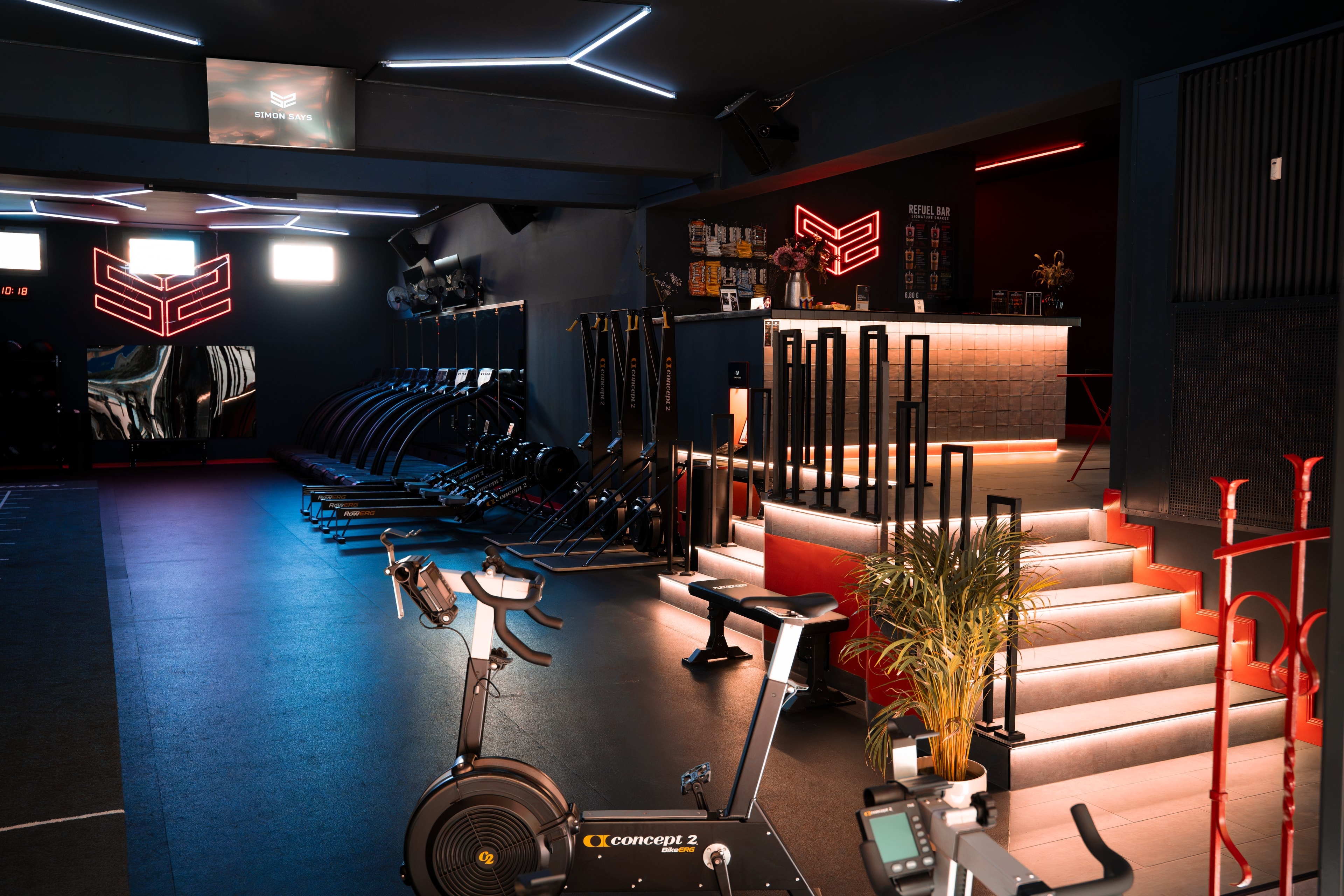 Studio mit Concept2 Bike, Treppe zur Refuel Bar und Neon-Signet